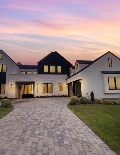 Modern two-story house with large windows, a stone and stucco exterior, and a paved driveway at sunset.