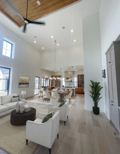 Modern open-concept living and dining area with high ceilings, light wood floors, neutral furniture, large windows, and a contemporary kitchen in the background.