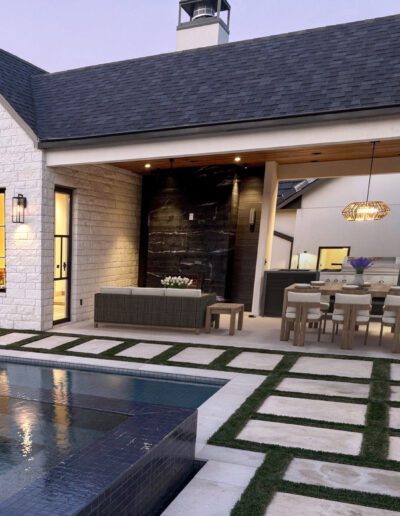 Modern house exterior with a covered patio, outdoor dining area, sectional sofa, swimming pool, and large windows at dusk.