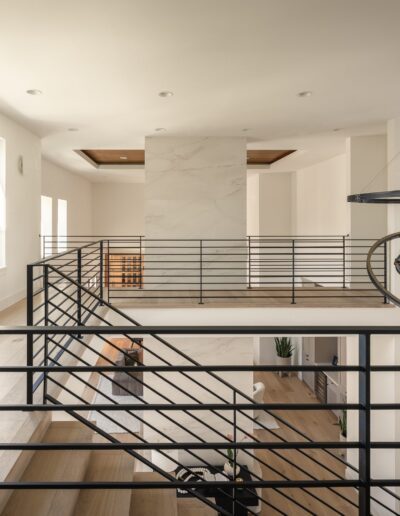 Modern interior with black metal railings, large windows, a marble accent wall, wooden floors, and contemporary circular light fixtures.