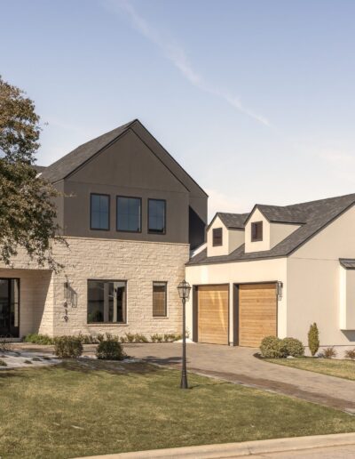 Modern two-story house with stone and stucco exterior, large windows, and a two-car garage, set on a landscaped lawn under a clear sky.