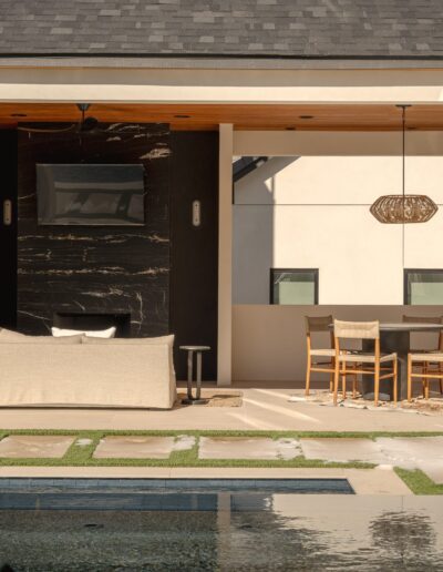Modern outdoor patio with a covered seating area, dining table with chairs, and a pool in the foreground. Neutral tones and clean architectural lines.