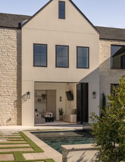 Modern two-story house with large windows, cream and stone exterior, open living room, and a backyard pool with geometric stepping stones leading to the entrance.